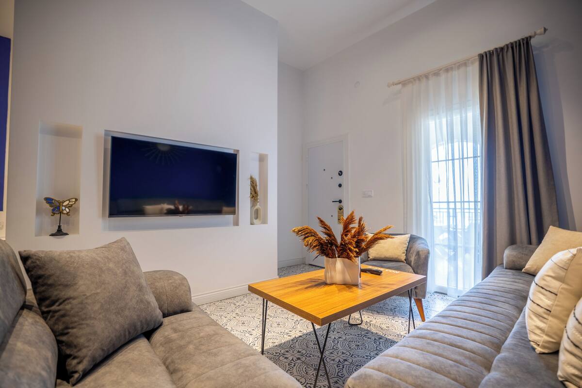 A modern living room with a sofa, a coffee table, and a flat-screen TV mounted on the wall.