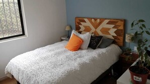 A bedroom with a bed, a wooden headboard, a window, a nightstand, a lamp, and a potted plant. - Great location in Barrio Italia, Providencia (Santiago)