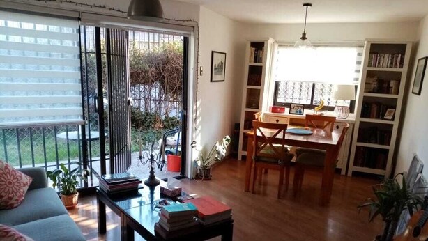 A living room with a sofa, coffee table, and books. There is a dining area with a table and chairs. A guitar is visible in the corner. - Great location in Barrio Italia, Providencia (Santiago)