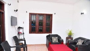 A room with a red table, two black leather chairs, a wooden cabinet, a TV, and a window with wooden frames. - Private House in Tangalle (Tangalle)