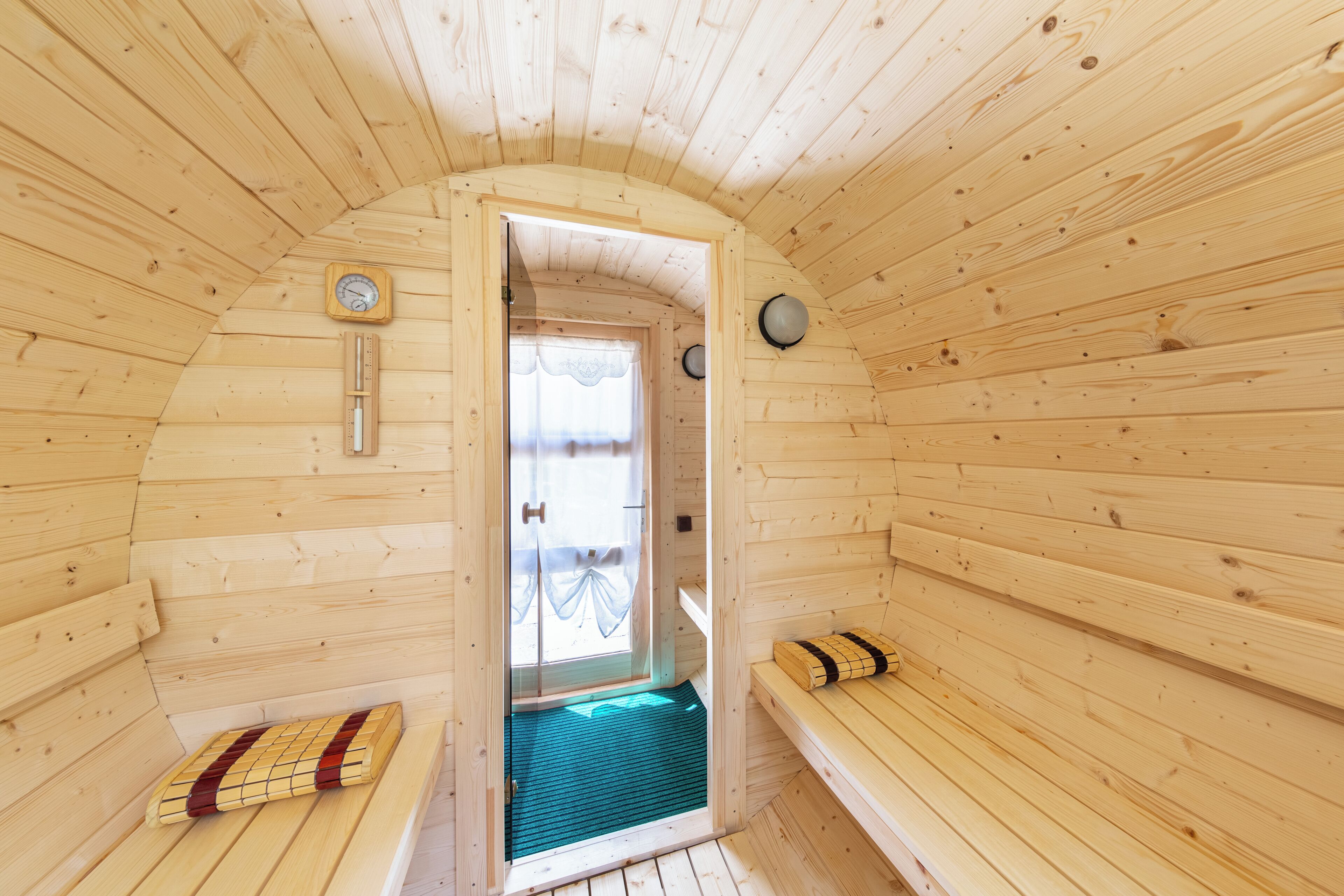 Une cabine de sauna en bois, avec des bancs, une porte et une horloge au mur.