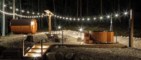 En træhytte med jacuzzi, udendørs siddepladser og lyskæder i en skov.