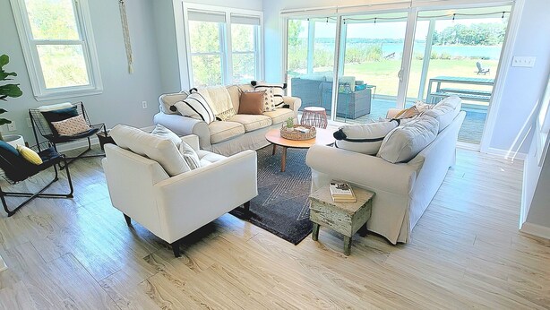 A spacious living room with a large window, a ceiling fan, and a view of the outdoors. - WATERFRONT!! **HOT TUB**  3 bedroom Oasis on 2+ acres - Sleeps 8 (Cambridge)