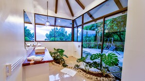 A modern bathroom with a wooden vanity, a large window, and a view of the outdoors. - Akua Ocean View Suites (Tárcoles)