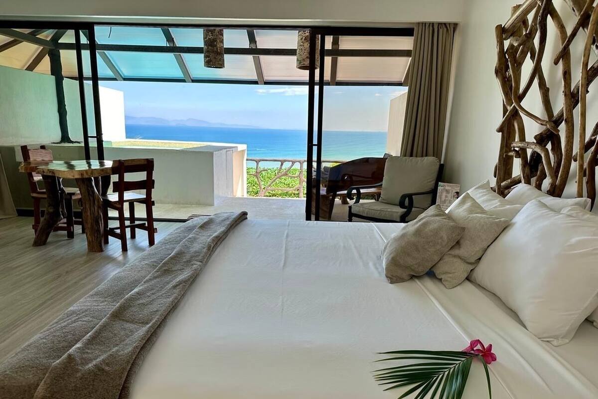A hotel room with a bed, a desk, and a view of the ocean.