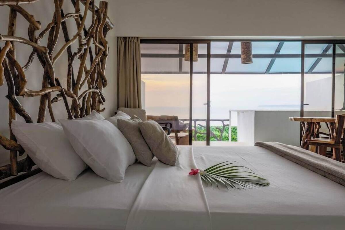 A hotel room with a bed, a view of the outdoors, and a wooden headboard.