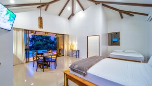 A modern bedroom with a large bed, a dining table, and chairs. There is a view of trees through the window. - Akua Ocean View Suites (Tárcoles)