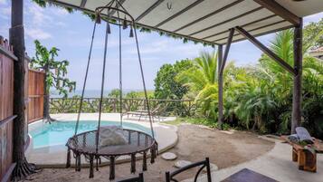 A covered outdoor area with a pool, a swing chair, and a wooden table.