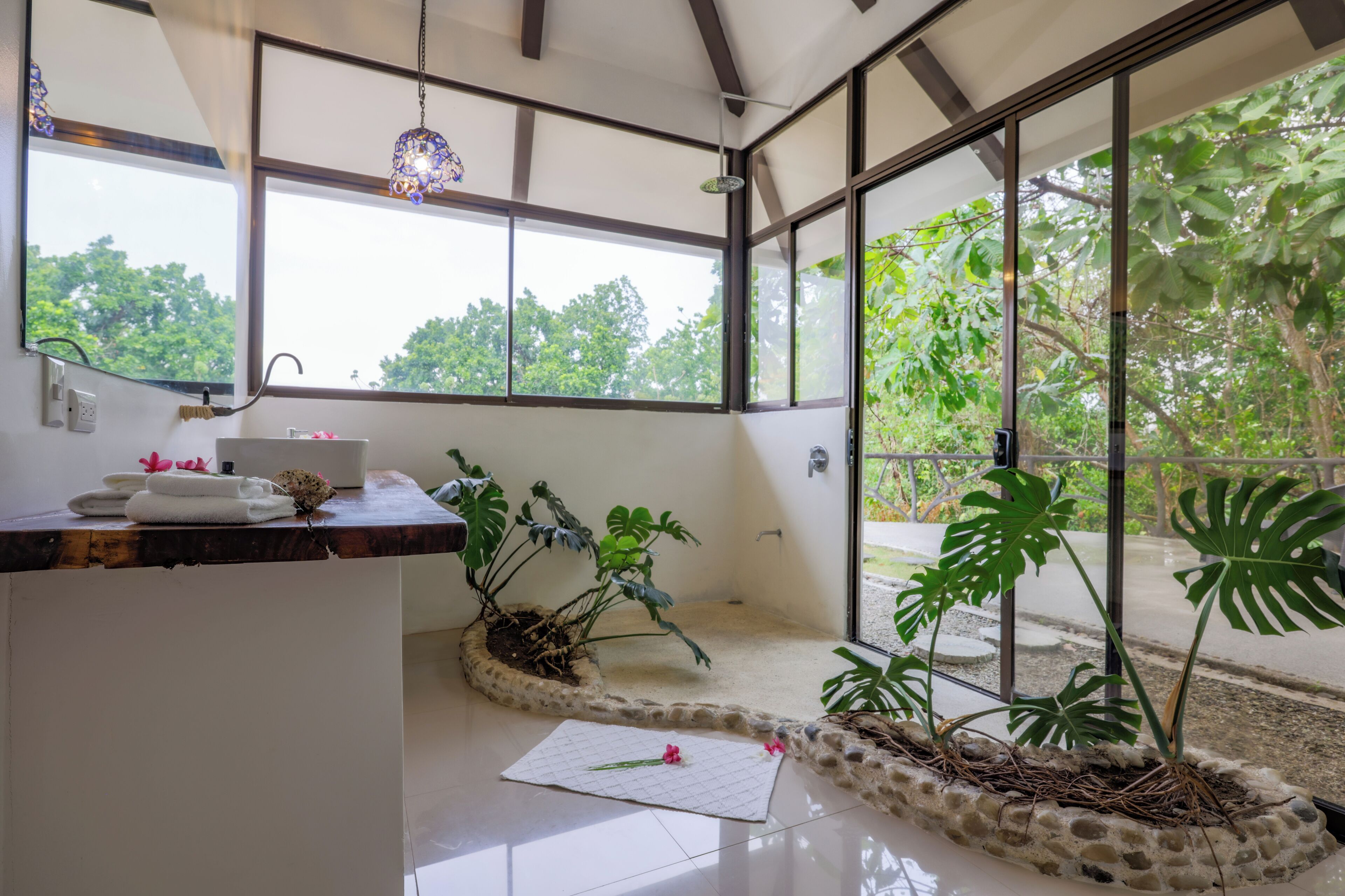 A modern bathroom with a large window, a sink, and a plant arrangement.