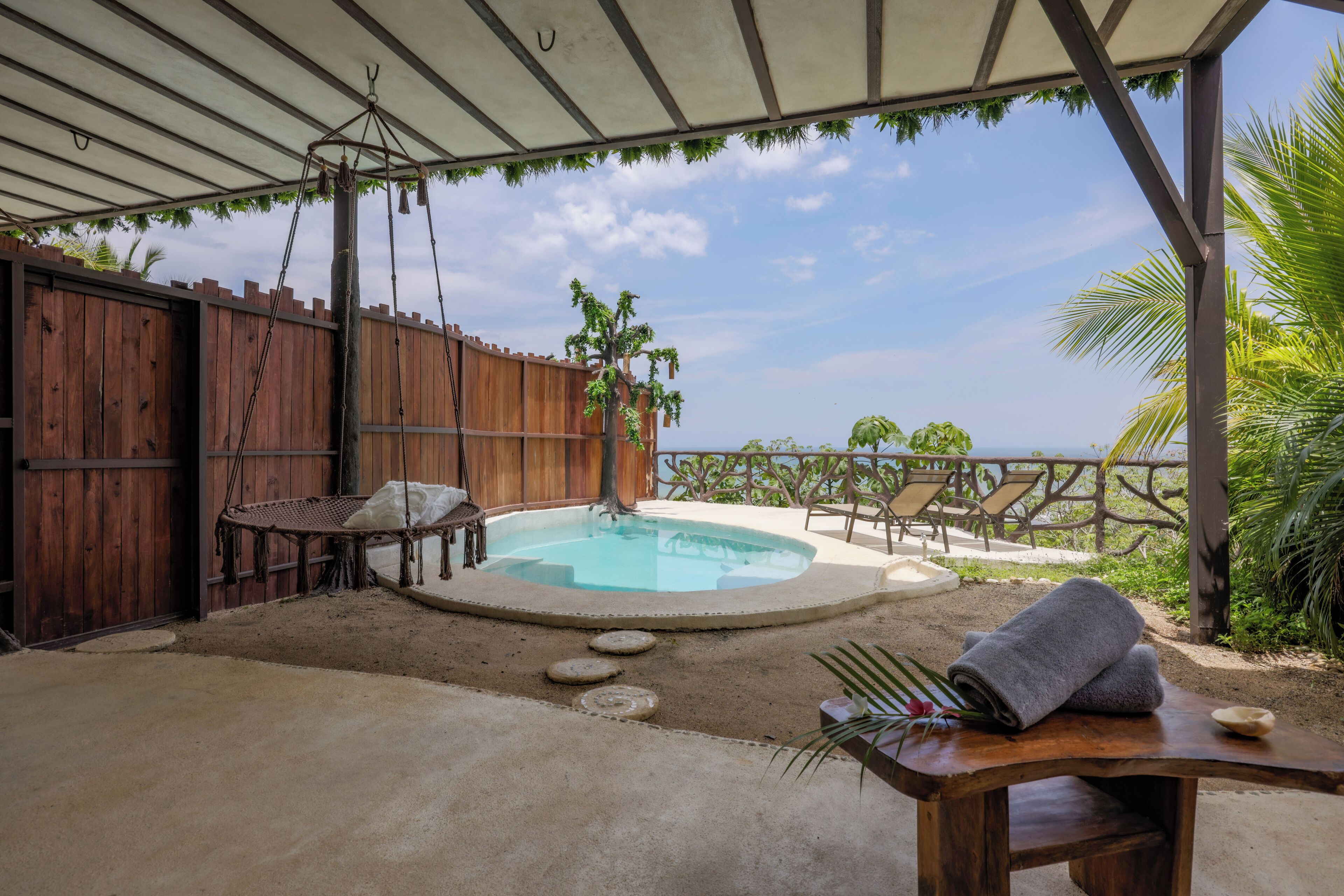 A covered outdoor area with a pool, wooden furniture, and a view of the ocean.