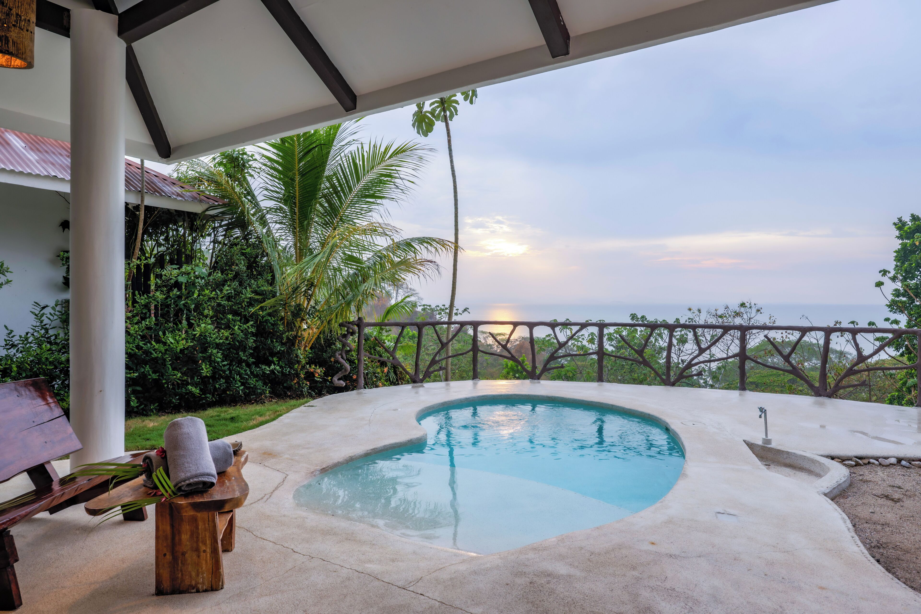 A pool area with a view of the ocean, a wooden bench with towels, and a pergola structure.