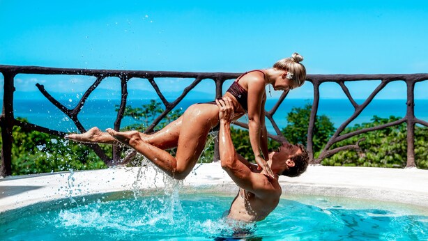 A man and woman in a swimming pool with a clear view of the ocean and a balcony railing. - Akua Ocean View Suites (Tárcoles)