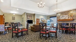 A hotel lobby with a carpeted floor, wooden chairs, a fireplace, and a television.