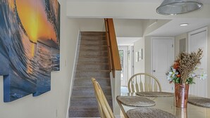 A dining area with a glass table, woven placemats, and a copper vase with flowers. A staircase with wooden steps leads to another room. - Pet Friendly, 3Bed, easy walk to Pool, Beach, Restaurants, Golf N Pickle Ball  (Edisto Island)