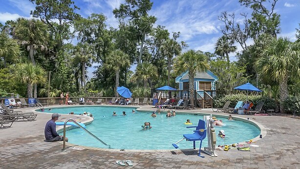 A pool area with lounge chairs and umbrellas, surrounded by palm trees. - Pet Friendly, 3Bed, easy walk to Pool, Beach, Restaurants, Golf N Pickle Ball  (Edisto Island)