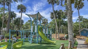 A playground with a slide and climbing structures, surrounded by palm trees and a clear sky. - Pet Friendly, 3Bed, easy walk to Pool, Beach, Restaurants, Golf N Pickle Ball  (Edisto Island)