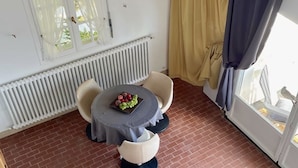 A room with a brick floor, a round table with chairs, a radiator, and a window with curtains.