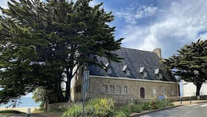 A stone building with a sloped roof, surrounded by trees and a clear sky.