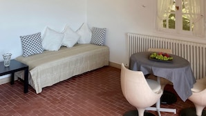 A cozy room with a wooden staircase, a sofa with patterned cushions, a small table with a fruit bowl, and a radiator.