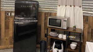 A compact kitchenette with a black Galanz refrigerator, a microwave, and a small shelf with dishes and a coffee maker.