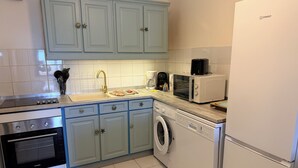 A kitchen with a dishwasher, washing machine, microwave, and a refrigerator. - À 10 mn à Pied de la Plage, T3 Jardin vue mer (Les Anses-d'Arlet)