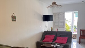 A living room with a sofa, a coffee table, and a television mounted on the wall. - À 10 mn à Pied de la Plage, T3 Jardin vue mer (Les Anses-d'Arlet)