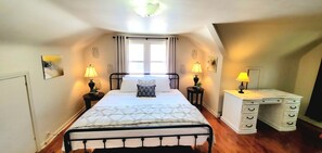 Un dormitorio con cama, lámparas de noche, un escritorio y una ventana con cortinas.