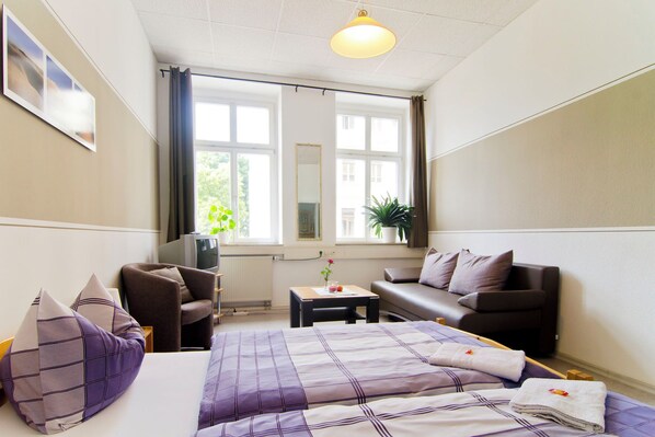 Une chambre d’hôtel avec un lit, un canapé, une télévision, une petite table et une fenêtre avec des rideaux.