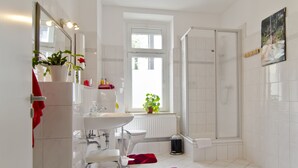 Ein modernes Badezimmer mit einem weißen Waschbecken, Spiegel und Toilette, einem Duschbereich und einem Fenster mit Pflanzen.