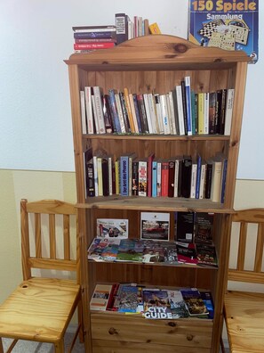 A wooden bookshelf with multiple shelves filled with books and magazines, flanked by two wooden chairs. - Pension Piano Forte (Leipzig)