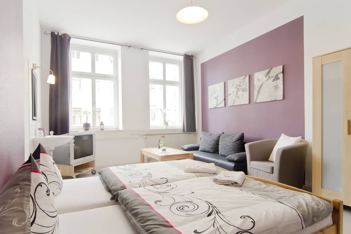 Habitación de hotel con dos camas, un sofá, un televisor y obras de arte en la pared.