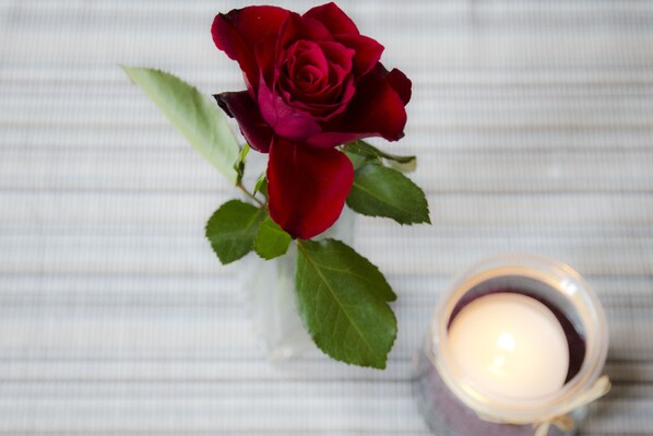 Une seule rose rouge, avec ses feuilles vertes, et une bougie dans un porte-bougie en verre, le tout posé sur une surface à rayures.