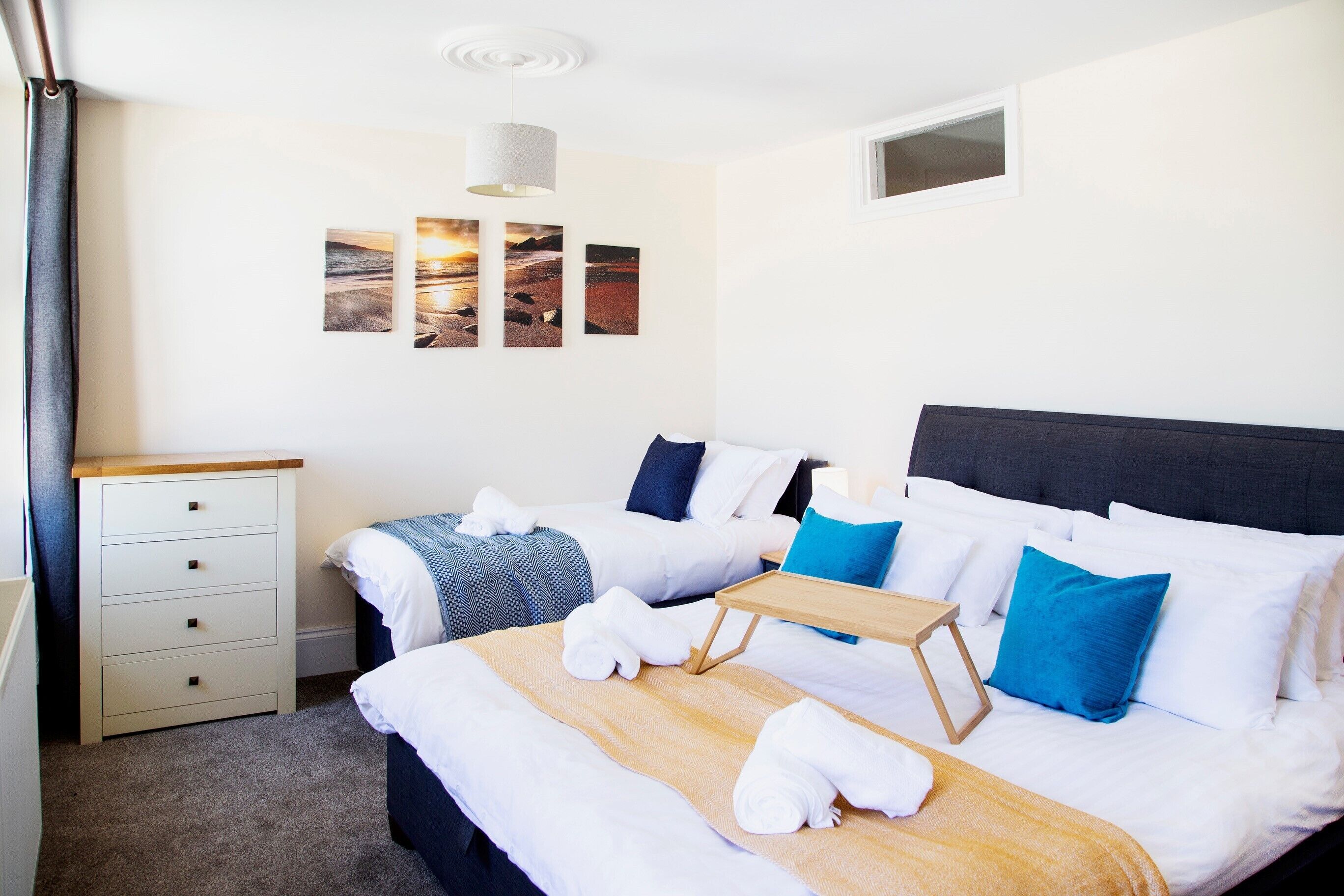 Une chambre d’hôtel avec deux lits, une table de chevet en bois, une petite table et une commode.