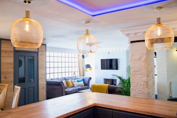 Una sala de estar moderna con una mesa de comedor de madera, un sofá gris con cojines coloridos y un amplio ventanal.