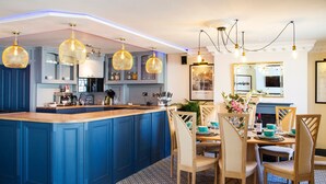 Una cocina moderna con una isla azul, luces colgantes y un comedor con sillas y mesa de madera.