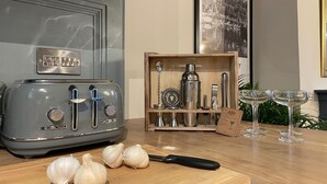 Una cocina con un tostador antiguo, una caja de madera con utensilios de cocina y una tabla de cortar con dientes de ajo.