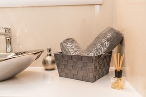 A bathroom with a modern sink, a decorative basket with towels, a bottle of liquid soap, and a reed diffuser. - Villa Rossa (Pasman)