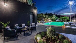 Une terrasse extérieure moderne, dotée d’une piscine, d’un espace salon et d’un éclairage soigné.