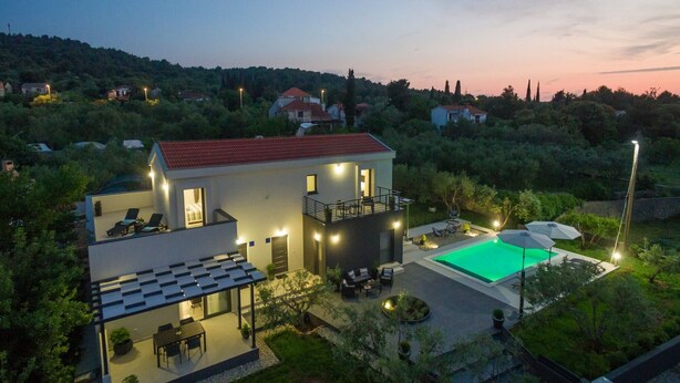 Une maison moderne à deux étages, dotée d’une terrasse sur le toit, d’une piscine et d’un jardin bien entretenu.