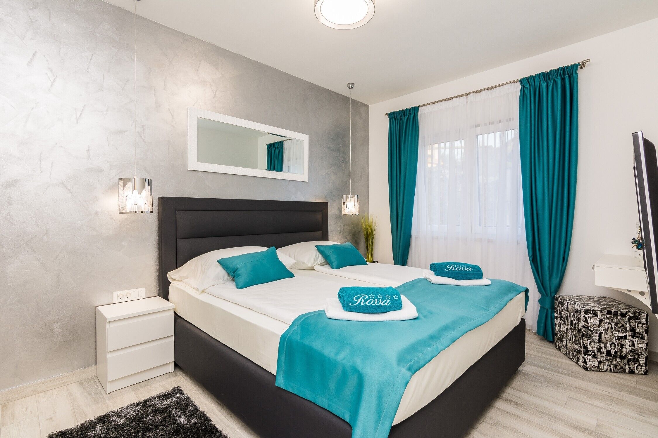 A modern bedroom with a large bed, a bedside table, a nightstand, a mirror, and a TV.