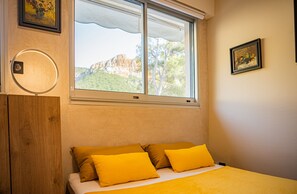 Ein Schlafzimmer mit Bett, zwei Kissen, einem Fenster mit Bergblick und einem gerahmten Bild an der Wand.