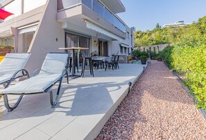 Ein modernes, zweistöckiges Gebäude mit einer Terrassenfläche, die Liegestühle und einen Tisch bietet.