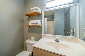 Et badeværelse med toilet, håndvask, spejl og en hylde med håndklæder.