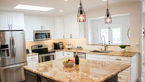 Una cocina moderna con gabinetes blancos, electrodomésticos de acero inoxidable, encimeras de granito e iluminación colgante.