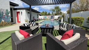 Un patio exterior con piscina, mobiliario de mimbre y un mural de cactus.