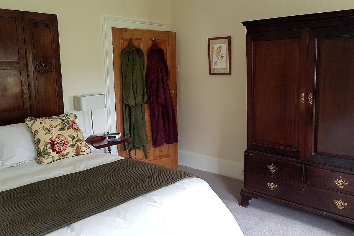 A bedroom with a bed, a wooden wardrobe, and a door with clothes hanging on it.