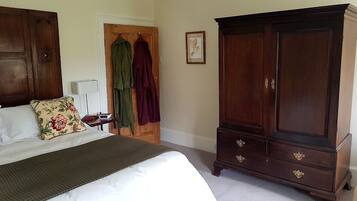 A bedroom with a bed, a wooden wardrobe, and a door with clothes hanging on it.
