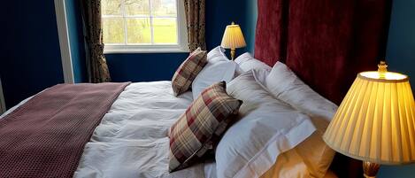 A neatly made bed with white linens and plaid pillows, a red throw blanket, and a bedside lamp.