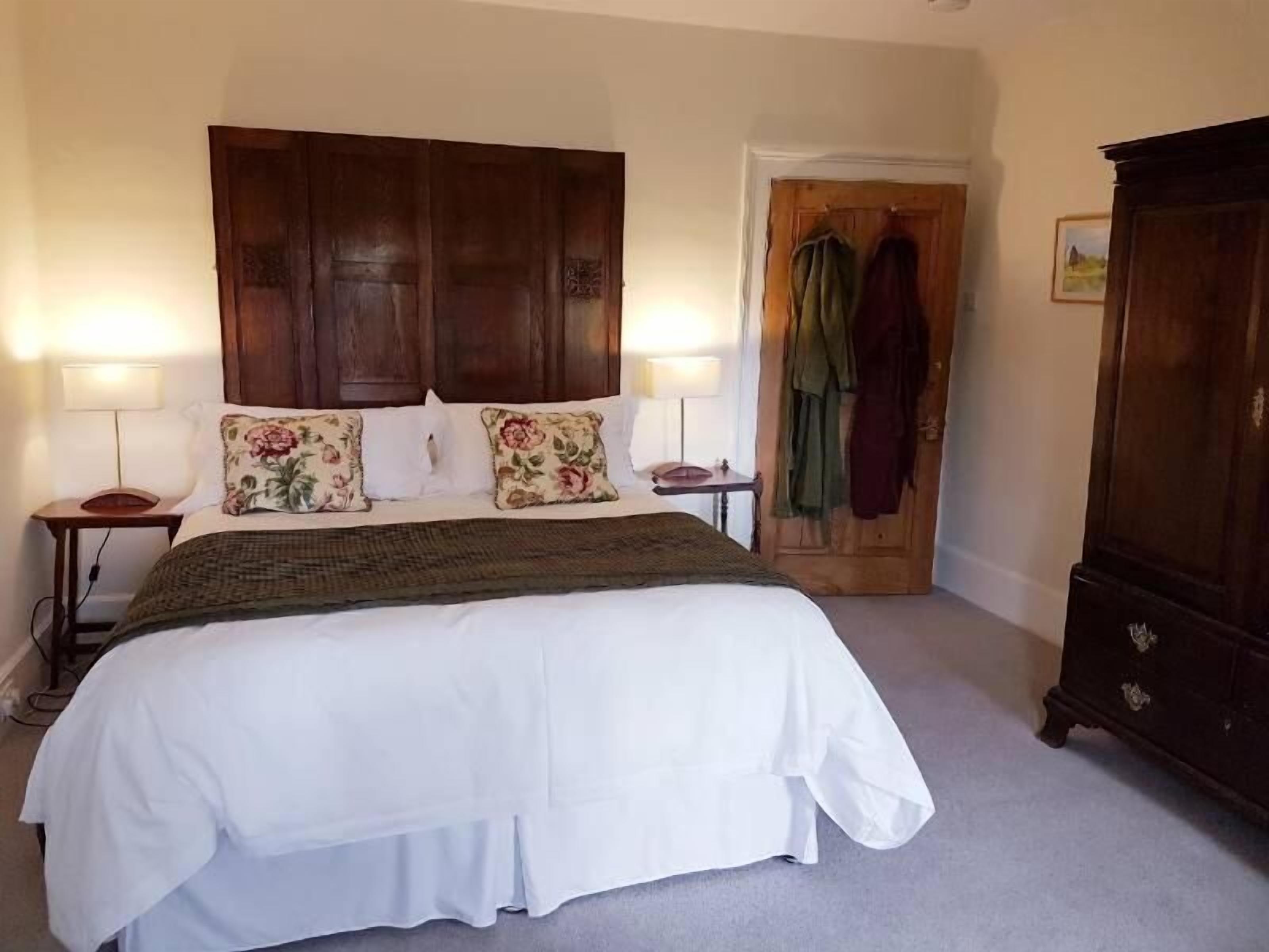 A bedroom with a large bed, two bedside tables, a wooden wardrobe, and a door leading to another room.