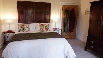 A bedroom with a large bed, two bedside tables, a wooden wardrobe, and a door leading to another room.